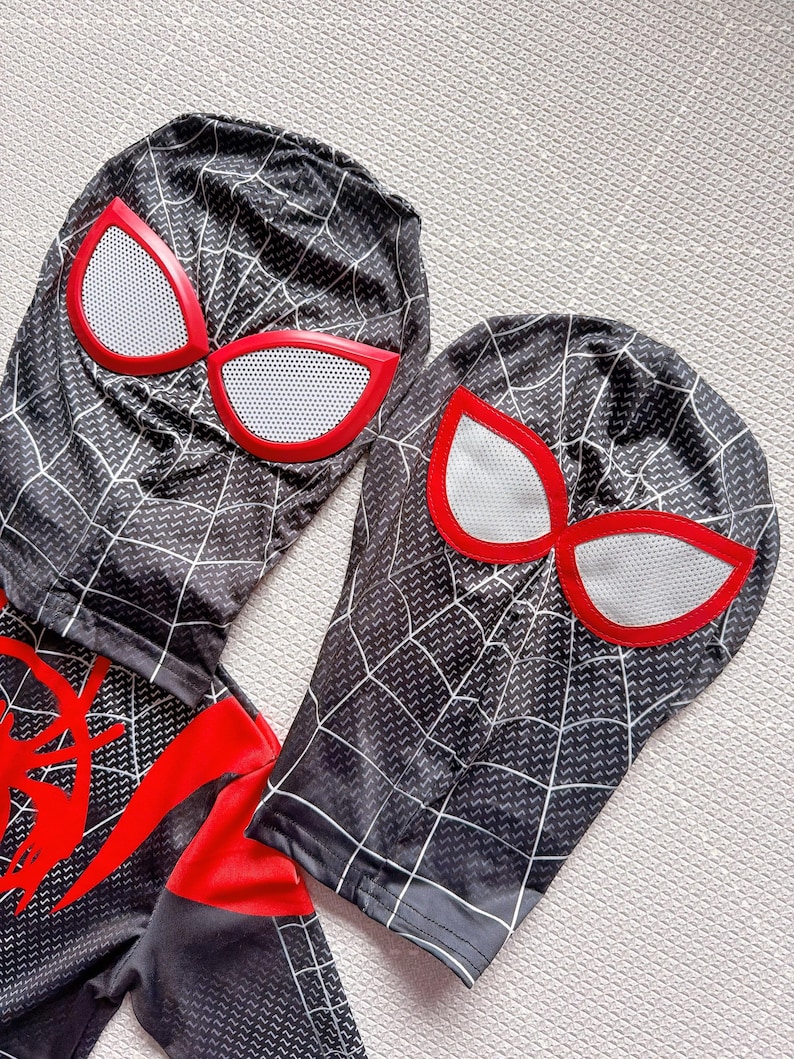 May include: Black and gray Spider-Man costume with white web detailing and red accents. The costume includes a hood with large red-rimmed eye shapes and a matching bodysuit. The design features a web pattern.