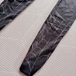 May include: Black leggings with a white spiderweb design. The leggings have a red accent at the bottom and a textured pattern throughout. The spiderweb design is on the front of the leggings.