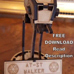 Op de afbeelding: Een houten model van een AT-ST Walker uit Star Wars. Het model is geassembleerd en staat op een basis met de woorden "AT-ST WALKER" erop gedrukt. De tekst in de afbeelding luidt "DIGITAAL BESTAND DOWNLOAD GRATIS DOWNLOAD Lees Beschrijving GEEN FY SIEK PRODUCT".