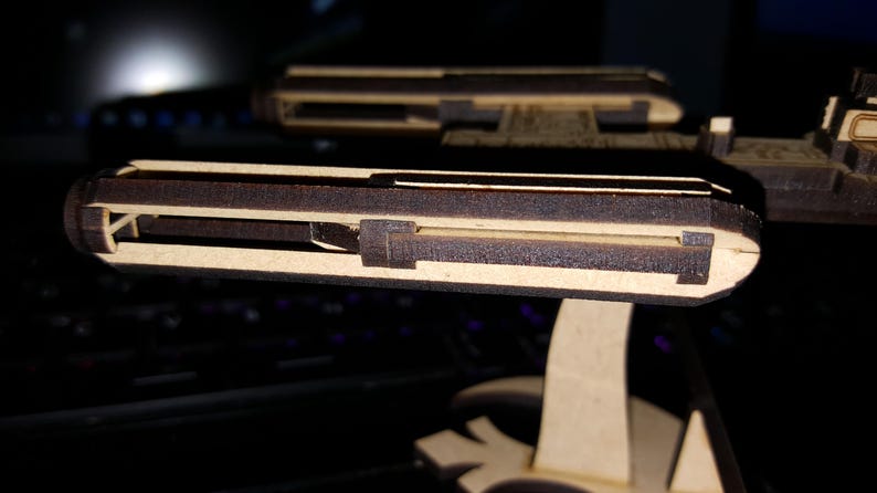 May include: A wooden model of a spaceship with a detailed interior. The model is made of light brown wood and has a dark brown paint finish. The spaceship has a long, narrow body with a pointed nose and a large, flat wingspan.
