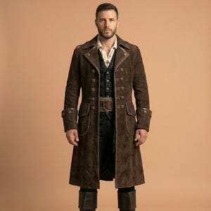 Puede incluir: Un abrigo largo de ante marrón con botones dorados y cinturón. El abrigo tiene puños decorativos y un corte entallado. El modelo lleva un chaleco y una camisa con cuello debajo. El abrigo llega hasta las rodillas.