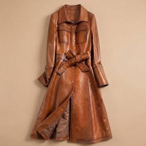 May include: A long, brown leather coat with a belted waist and button-down front. The coat features two chest pockets and a classic collar. The coat is approximately 55 inches long.