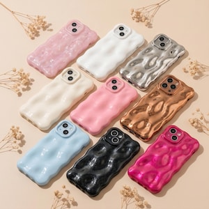 Puede incluir: Una colección de nueve fundas para smartphone con una textura ondulada similar a un líquido. Las fundas están disponibles en varios colores, incluyendo rosa claro, blanco, plata metalizada, crema, rosa sólido, bronce metalizado, azul claro, negro y fucsia.