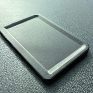 May include: A rectangular, dark grey tray with a slightly raised rim. The tray has a textured surface and rounded corners. The tray is on a textured, dark grey surface.