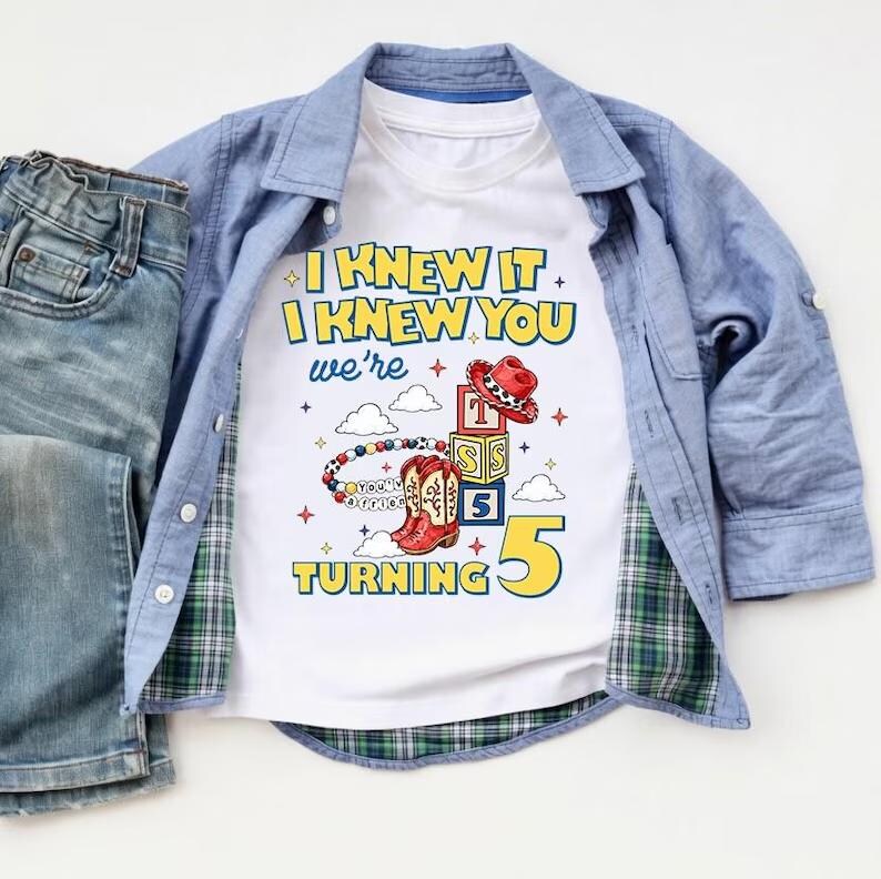 Op de afbeelding: Een wit t-shirt met de tekst I KNEW IT I KNEW YOU we're TURNING 5, voorzien van afbeeldingen van een rode cowboyhoed, alfabetblokken, een kralenarmband en rode cowboylaarzen. Het t-shirt wordt gedragen onder een blauw overhemd en een blauwe spijkerbroek.