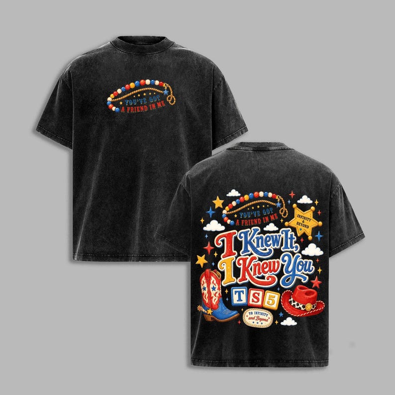 May include: A black acid-wash t-shirt featuring a front graphic of a beaded lasso and the text "You've Got A Friend In Me." The back displays a colorful design with a cowboy boot, hat, stars, clouds, and the text "I Knew It, I Knew You TS5."