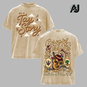 May include: A beige mineral-washed t-shirt featuring a front graphic with rope-style text reading 'it's a Tay Story' and clouds. The back graphic displays 'Cowgirl like Me' in rope text, a guitar, a hat, and the text 'Takes One to Know One'.