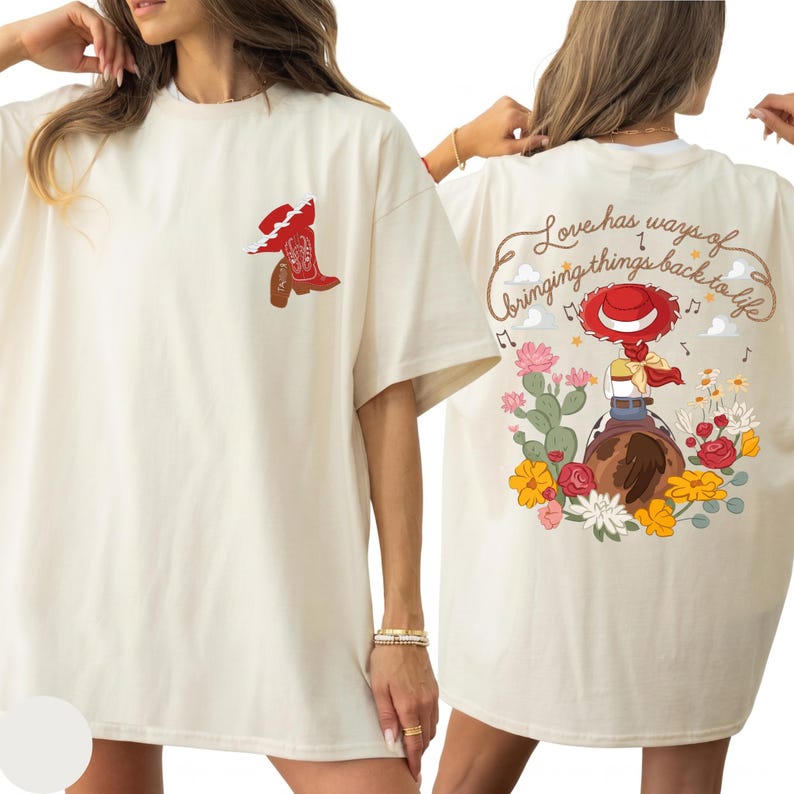 May include: An off-white t-shirt featuring a small red cowboy boot graphic on the front left chest. The back displays a colourful illustration of a cowgirl on a horse surrounded by cacti and flowers, with the text Love has ways of bringing things back to life.