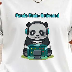Op de afbeelding: Wit T-shirt met een gepixeleerde panda met een koptelefoon op en een videogame aan het spelen. De tekst "Panda Mode: Activated" staat boven de panda. De panda is zwart, wit en grijs, met een turquoise spelconsole.