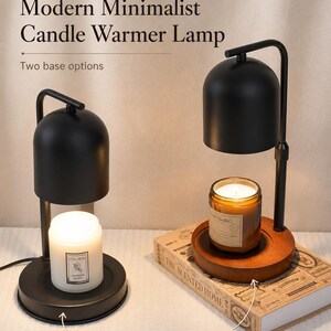 May include: Two candle warmer lamps with black dome shades and curved metal arms. One lamp features a black wrought iron base with a white candle, while the other has a round walnut wood base holding an amber glass candle jar with a lit wick.