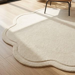 May include: A cream-colored area rug with a scalloped, cloud-like edge and a textured, plush surface. The rug features a distinct border following the curved perimeter, creating a soft, organic shape that rests flat on the floor surface.