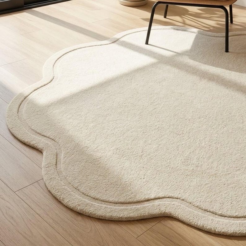 May include: A cream-colored area rug with a scalloped, cloud-like edge and a textured, plush surface. The rug features a distinct border following the curved perimeter, creating a soft, organic shape that rests flat on the floor surface.