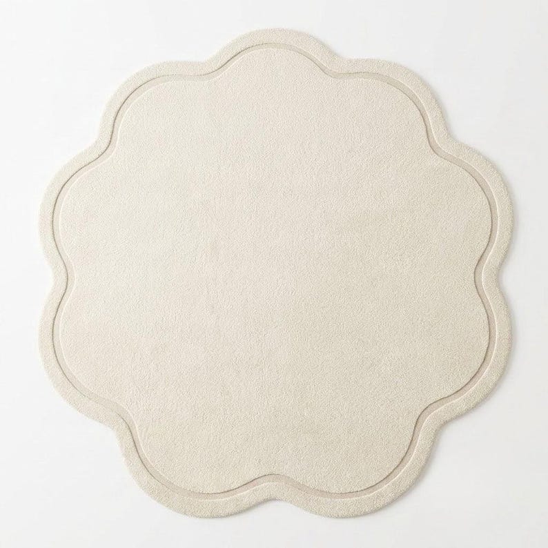 Top view of a soft cream scalloped flower-shaped rug showing its unique curved silhouette, neutral color, and elegant minimalist design. 🌸🤍