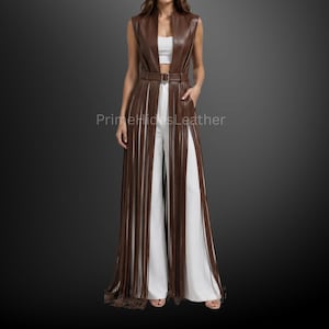 May include: A sleeveless brown leather vest featuring a high collar, a waist belt with a buckle, and long vertical fringe panels extending to the floor. The vest is worn over a white crop top and white wide-leg trousers. Text reads PrimeHidesLeather.