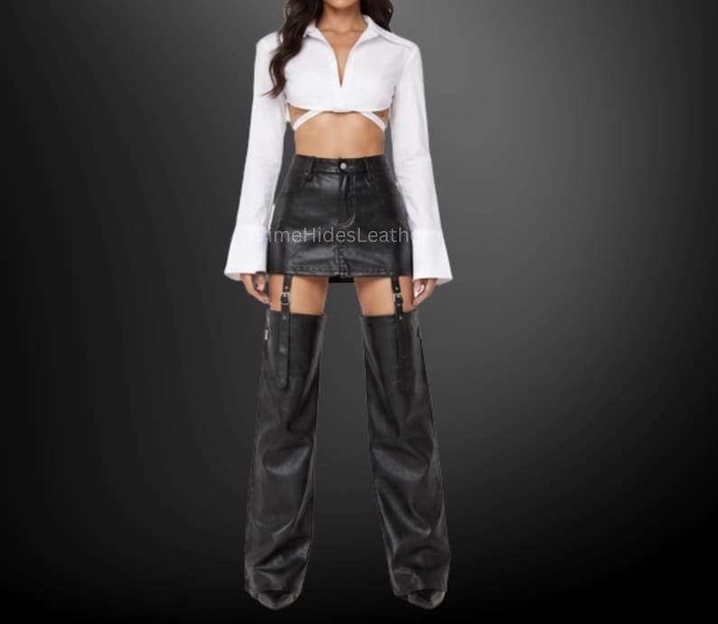 May include: A white long-sleeved cropped shirt with a collar and wrap-around waist ties, paired with a black leather mini skirt and matching black leather leg warmers that attach to the skirt with vertical buckled straps and metal hardware.