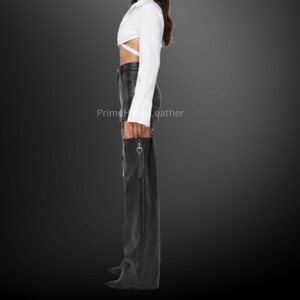 May include: A white long-sleeved cropped shirt with wrap-around waist ties paired with black leather shorts and matching black leather chaps featuring side zippers and silver hardware. The text PrimeHideLeather is visible on the image.