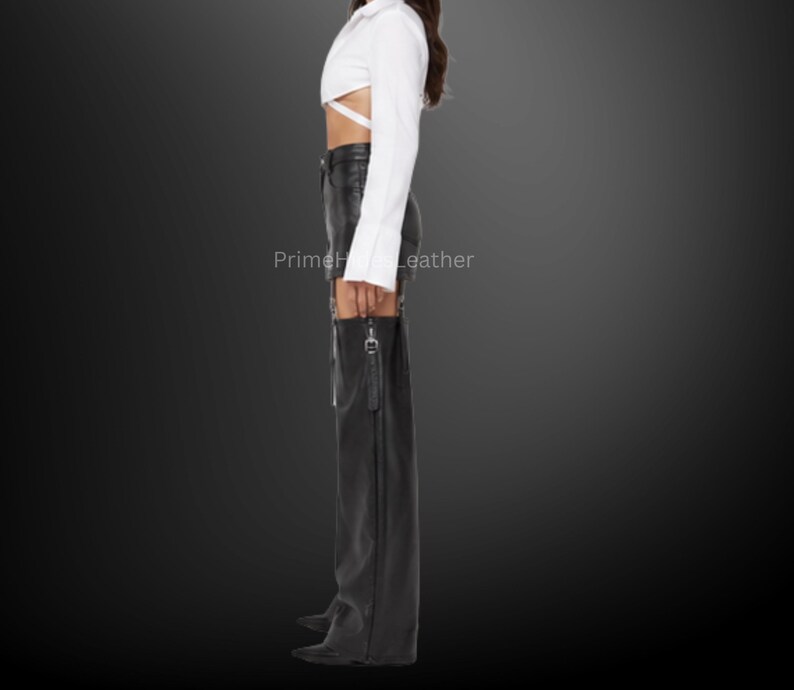 May include: A white long-sleeved cropped shirt with wrap-around waist ties paired with black leather shorts and matching black leather chaps featuring side zippers and silver hardware. The text PrimeHideLeather is visible on the image.