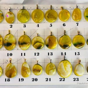 May include: A collection of 24 handcrafted glass pendants in various shapes and sizes. The pendants are primarily yellow with gold-colored bails. Some pendants have green or black accents. Each pendant is numbered for easy selection.