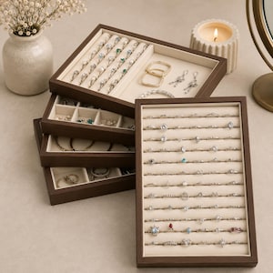 May include: A collection of dark wood jewelry boxes with multiple compartments and drawers. The boxes are filled with rings, earrings, bracelets, and other jewelry. The jewelry includes gold and silver pieces with various gemstones and pearls. A lit candle and vase of flowers are in the background.