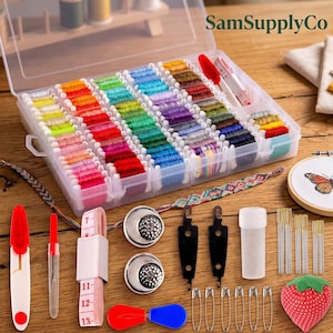 May include: A clear plastic storage box filled with colorful embroidery floss bobbins, a measuring tape, two metal thimbles, two black needle threaders, a needle case, sewing needles, safety pins, a strawberry pincushion, and a seam ripper.