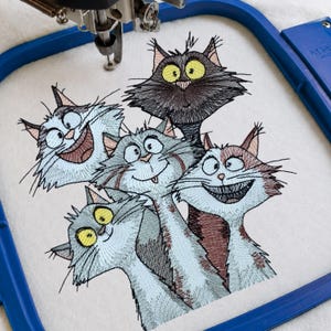 Könnte beinhalten: Gesticktes Design von fünf Cartoon-Katzen mit übertriebenen Gesichtsausdrücken. Die Katzen sind in Grau-, Braun- und Schwarztönen gehalten, mit gelben Augen und breiten Grinsen. Das Design befindet sich auf einem weißen Stoff, der in einem blauen Stickrahmen gehalten wird.