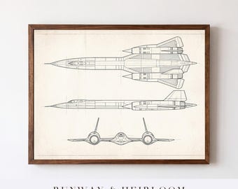 Puede incluir: Una impresión de dibujo técnico enmarcada que presenta tres proyecciones ortográficas de un avión Lockheed SR-71 Blackbird en líneas negras sobre un fondo crema. La obra está encerrada en un marco de madera marrón oscuro y rectangular.