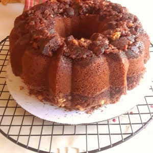 May include: A brown bundt cake with a chocolate glaze and nuts on top, sitting on a wire rack.