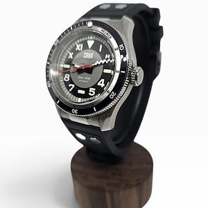 Puede incluir: Un reloj autom&aacute;tico negro y plateado con correa de caucho negra. La esfera presenta n&uacute;meros ar&aacute;bigos blancos, un segundero rojo y el texto "SQUALE" y "200m-660ft AUTOMATIC". El bisel incluye los textos "MINUTES" y "HEURES" impresos.