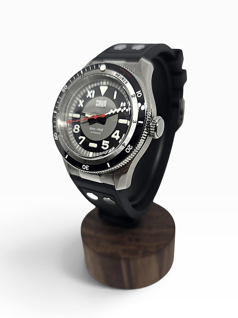 Puede incluir: Un reloj autom&aacute;tico negro y plateado con correa de caucho negra. La esfera presenta n&uacute;meros ar&aacute;bigos blancos, un segundero rojo y el texto "SQUALE" y "200m-660ft AUTOMATIC". El bisel incluye los textos "MINUTES" y "HEURES" impresos.
