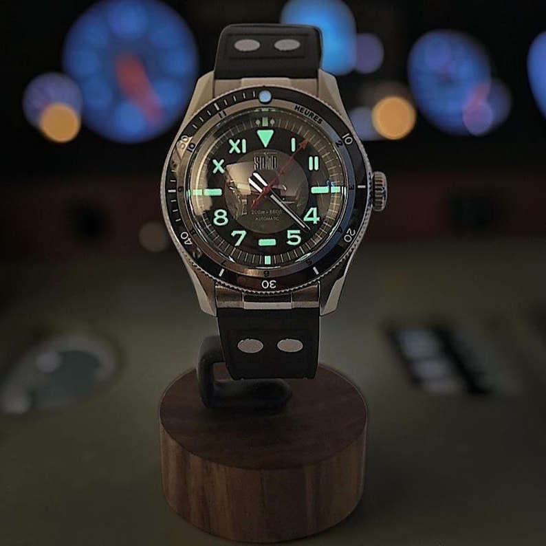 Puede incluir: Un reloj de pulsera autom&aacute;tico de acero inoxidable con esfera negra, marcadores de hora luminosos y correa de caucho negra. La esfera presenta el texto "SOLO" en la parte superior, n&uacute;meros ar&aacute;bigos 4, 5, 7, 8, 10, 11 y un bisel giratorio "HEURES".