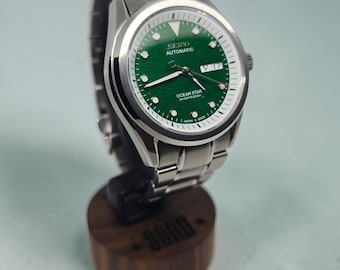 Puede incluir: Un reloj de pulsera de acero inoxidable en tono plateado con una esfera verde texturizada, que presenta el texto SEIKO AUTOMATIC y OCEAN STAR DIVER'S 200M. El reloj tiene una ventana de día y fecha a las tres, manecillas luminosas y brazalete.