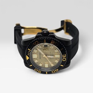 Pu&ograve; includere: Un orologio da polso Seiko con cassa nera e quadrante dorato testurizzato con indicatori luminosi. L'orologio presenta un cinturino in gomma nera con chiusura deployante dorata e una ghiera nera girevole con numeri e indici color oro.