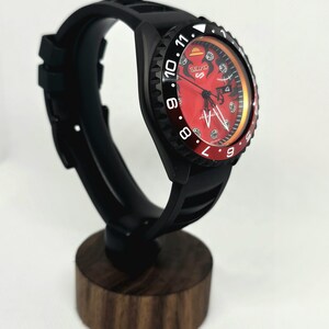 May include: A Seiko 5 Sports automatic watch with a black case and silicone strap. The dial is red with a straw hat icon at the twelve o'clock position, black indices, and a date window. The bezel is black and red with white numerals.