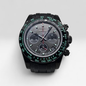 May include: A black Seiko chronograph watch with a dark grey dial, three sub-dials, and a tachymeter bezel featuring teal-colored numbers and the text UNITS PER HOUR. The watch includes a date window at the four o'clock position and silver hands.