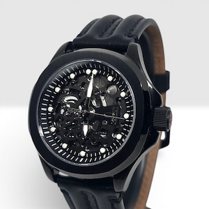 May include: A black Seiko wristwatch with a skeleton dial revealing the internal mechanical movement. The watch features a round black case, white hour markers, silver hands, and a black leather strap with prominent raised vertical stitching.