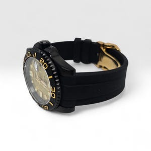Pu&ograve; includere: Un orologio da polso nero con quadrante dorato testurizzato, ghiera girevole nera con numeri color oro e cinturino in silicone nero con chiusura in metallo dorato. Il quadrante mostra il marchio Seiko e una finestrella per la data.