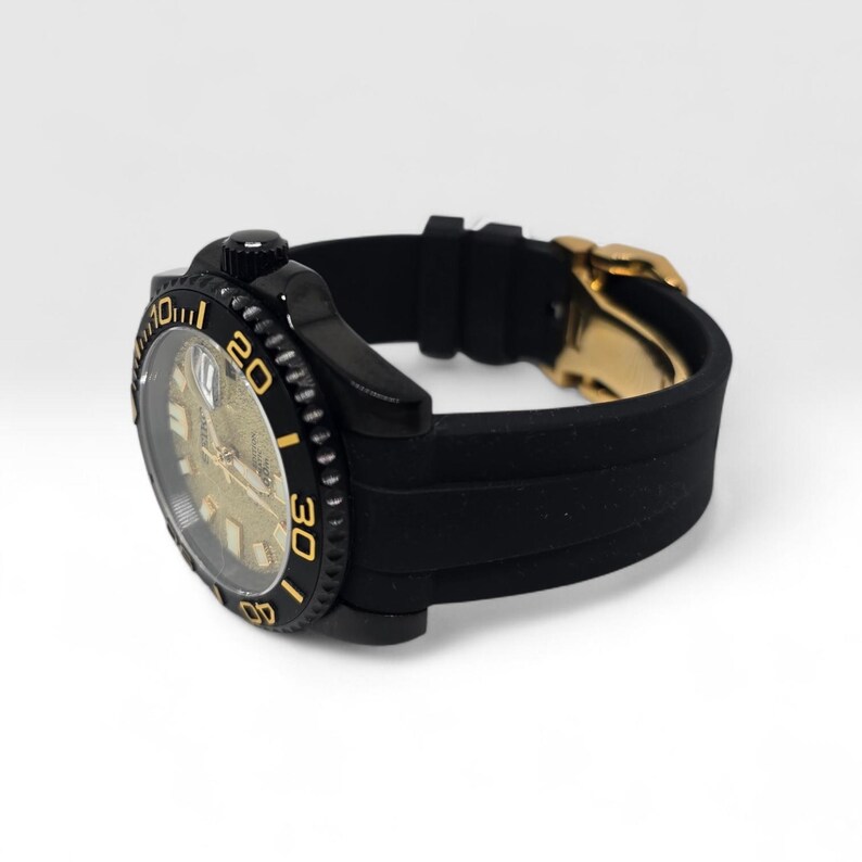 Pu&ograve; includere: Un orologio da polso nero con quadrante dorato testurizzato, ghiera girevole nera con numeri color oro e cinturino in silicone nero con chiusura in metallo dorato. Il quadrante mostra il marchio Seiko e una finestrella per la data.