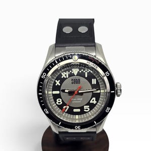 Puede incluir: Un reloj autom&aacute;tico de acero inoxidable con esfera negra, que presenta el nombre de la marca SOND, n&uacute;meros ar&aacute;bigos blancos 4, 5, 7, 8 y 11, un segundero rojo y un bisel giratorio negro con marcas blancas. Correa de caucho negra con dos remaches plateados.