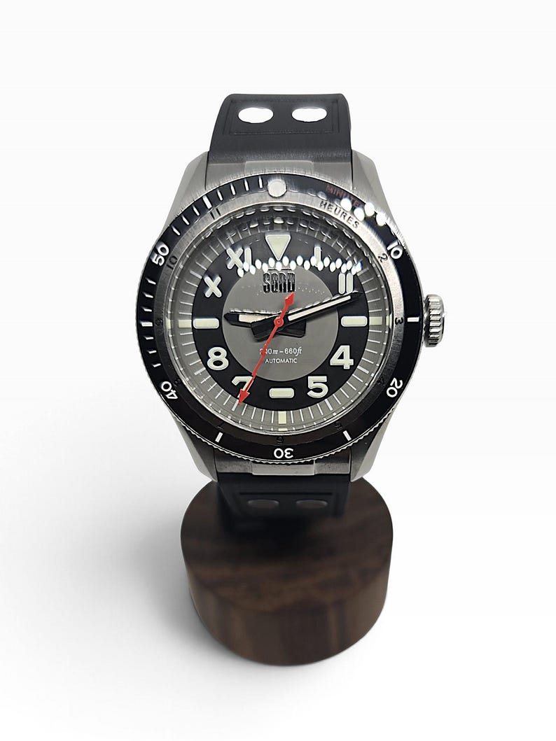 Puede incluir: Un reloj de pulsera autom&aacute;tico de acero inoxidable con correa de caucho negra y bisel giratorio negro. La esfera gris presenta n&uacute;meros ar&aacute;bigos blancos 4, 5, 8 y 11, un segundero rojo y el texto SORD, 200m-660ft, AUTOMATIC impreso en la cara.