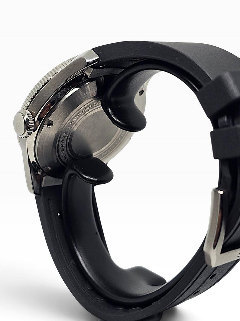 Puede incluir: Un reloj de pulsera con correa de caucho negra y caja de acero inoxidable plateado. Se observa la parte posterior de la caja, con detalles de metal cepillado circular y el texto SAPPHIRE CRYSTAL y WATER RESISTANT 200M.