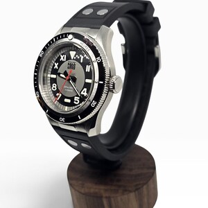 Puede incluir: Un reloj de pulsera autom&aacute;tico con correa de caucho negra que presenta dos remaches plateados. El reloj tiene una caja de acero inoxidable plateado, un bisel giratorio negro con marcas blancas y una esfera gris con el texto SORD, 200m-660ft y AUTOMATIC.