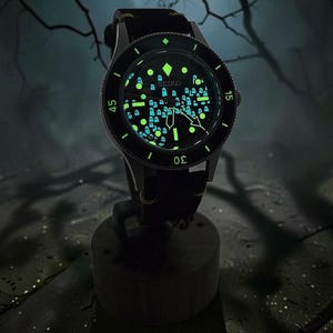 May include: A Seiko wristwatch with a black dial featuring a luminous pattern of small ghost figures. The watch has a black rotating bezel with white numerals, silver-tone hands, and a black strap. The dial markers and ghost shapes glow in the dark.