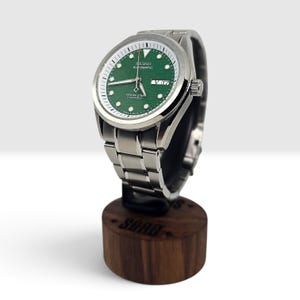 May include: A Seiko Automatic wristwatch with a textured green dial, silver-tone hands, and hour markers. The watch features a stainless steel link bracelet, a day-date window at the three o'clock position, and the text Ocean Star Diver's 200m.