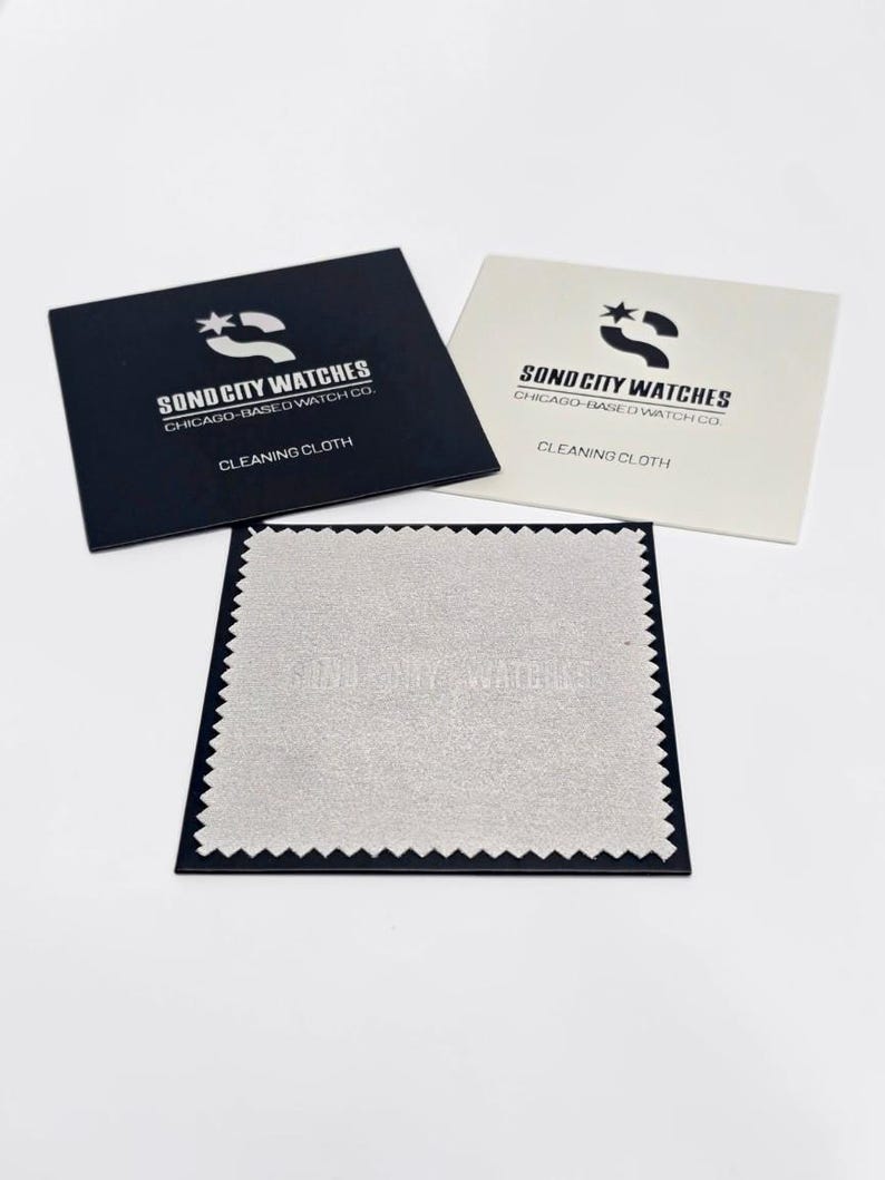 May include: A black square envelope, a white square envelope, and a light grey square cleaning cloth with pinked edges. Both envelopes feature the logo and text SOND CITY WATCHES CHICAGO-BASED WATCH CO. CLEANING CLOTH printed on them.
