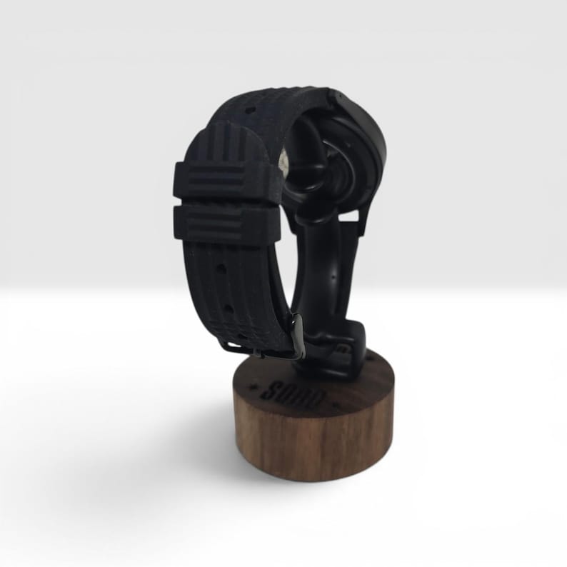 May include: A black silicone watch strap attached to a circular watch case, mounted on a cylindrical wooden stand. The base of the stand features the text SODO engraved on the side. The watch strap has a textured surface with a buckle closure.