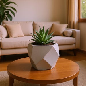 May include: A geometric, light gray concrete planter with a green succulent plant on a round, wooden coffee table. The planter has a faceted design. The background includes a beige sofa and neutral-toned curtains, creating a modern, minimalist aesthetic.