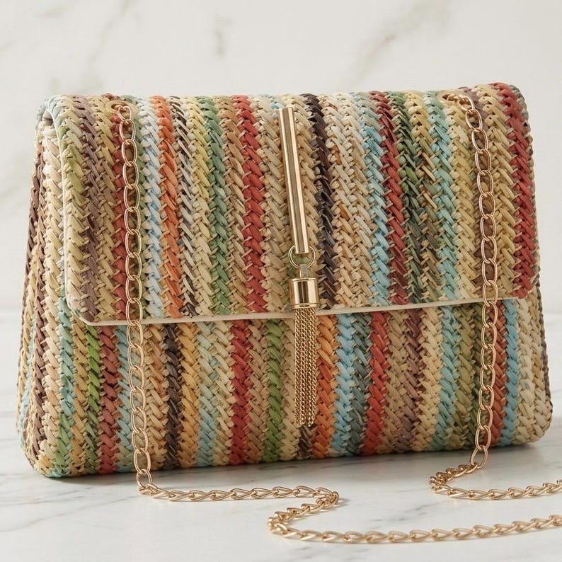K&ouml;nnte beinhalten: Eine rechteckige Clutch mit einem gewebten Streifenmuster in Beige-, Rot-, Gr&uuml;n- und Blaut&ouml;nen. Sie hat einen goldfarbenen Kettenriemen und ein goldfarbenes Quastendetail auf der Frontklappe. Die Tasche ist f&uuml;r den Transport von Essentials konzipiert.