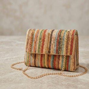 K&ouml;nnte beinhalten: Eine rechteckige Handtasche mit einem gewebten Streifenmuster in Braun-, Orange-, Gr&uuml;n- und Blaut&ouml;nen. Die Tasche hat einen goldfarbenen Kettenriemen und ein goldenes Quastendetail auf der Frontklappe. Die Tasche ist etwa 23 cm breit.