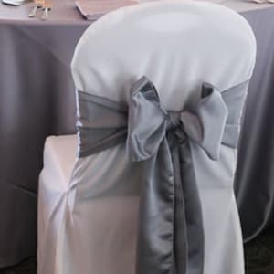 May include: A white chair cover with a silver satin sash tied into a bow.