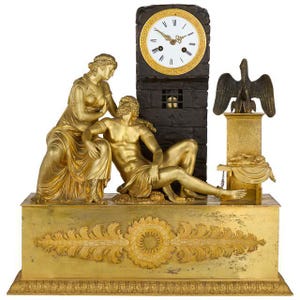 May include: A gold-toned mantel clock featuring a white clock face with black Roman numerals. The base displays ornate leaf carvings. Two gold figures are seated beside a dark stone-like clock tower, with a bronze eagle perched on a pedestal.